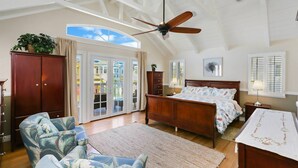 Ein geräumiges Schlafzimmer mit einem großen Bett, einem Deckenventilator und Blick durch die Glastüren.