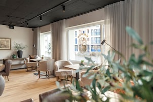 Una habitación de hotel moderna con piso de madera, un área de comedor con mesa y sillas, un ventanal con cortinas y vistas panorámicas de la ciudad.