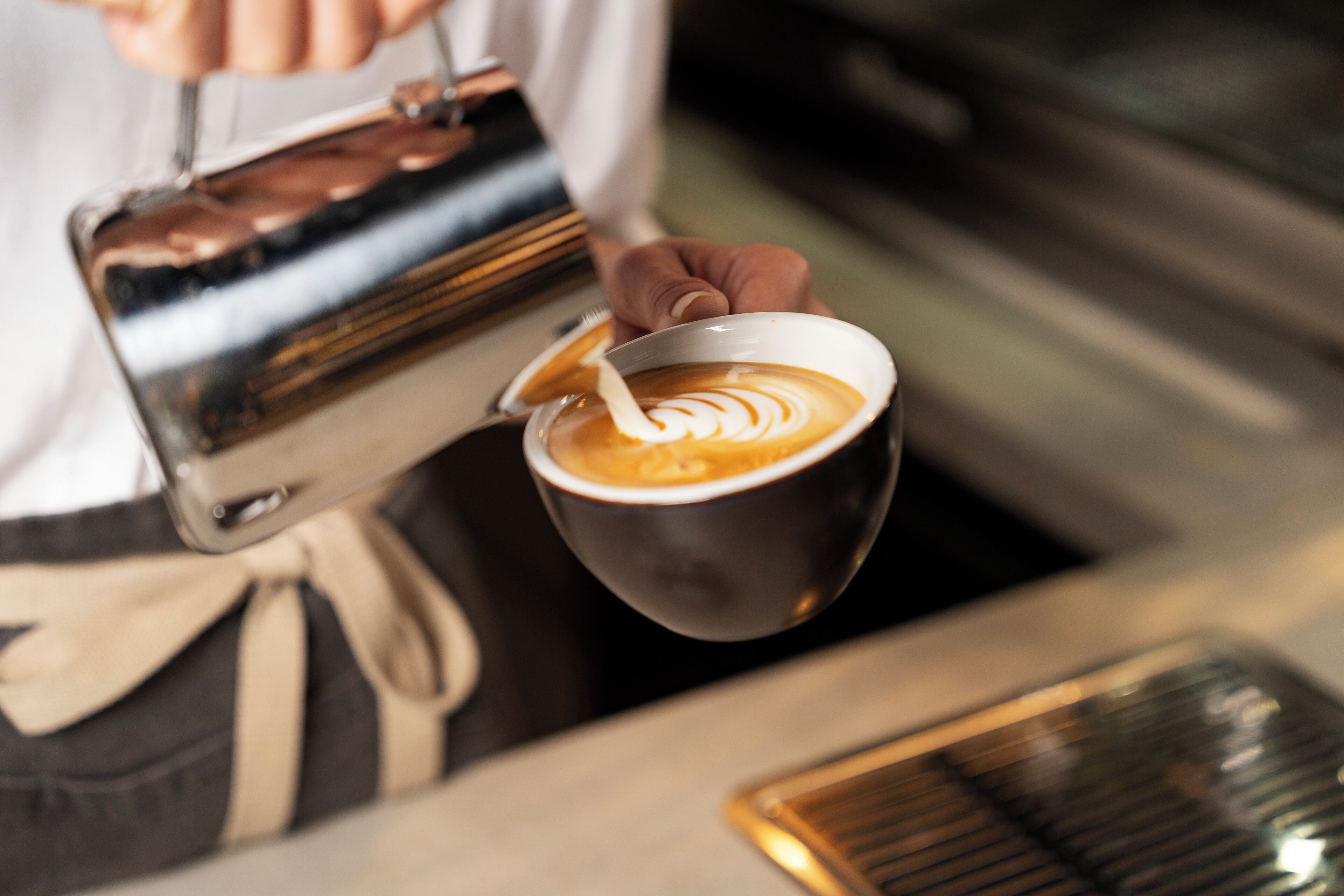 Un barista vertiendo leche al vapor en una taza de café, creando un diseño de arte latte.
