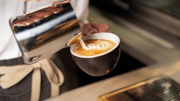 Un barista vertiendo leche al vapor en una taza de café, creando un diseño de arte latte.
