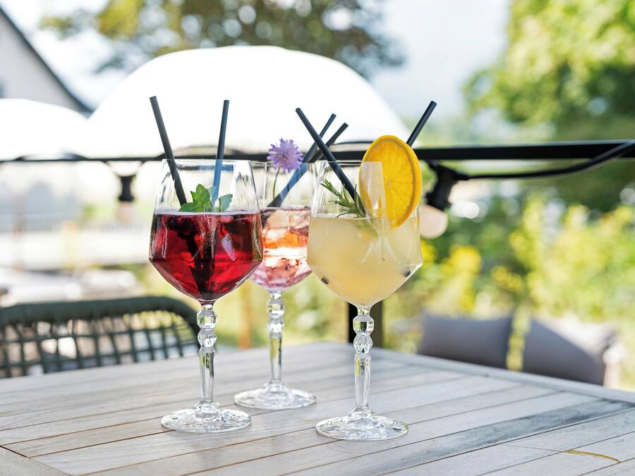 Three cocktails on a table with a view of greenery and a white building in the background.