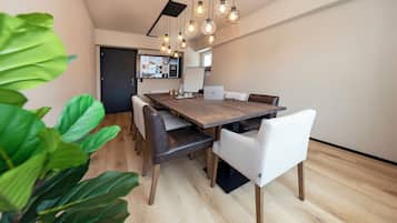 Uma sala de jantar moderna com uma mesa de madeira e cadeiras de couro, uma televisão na parede e uma planta em vaso em primeiro plano.