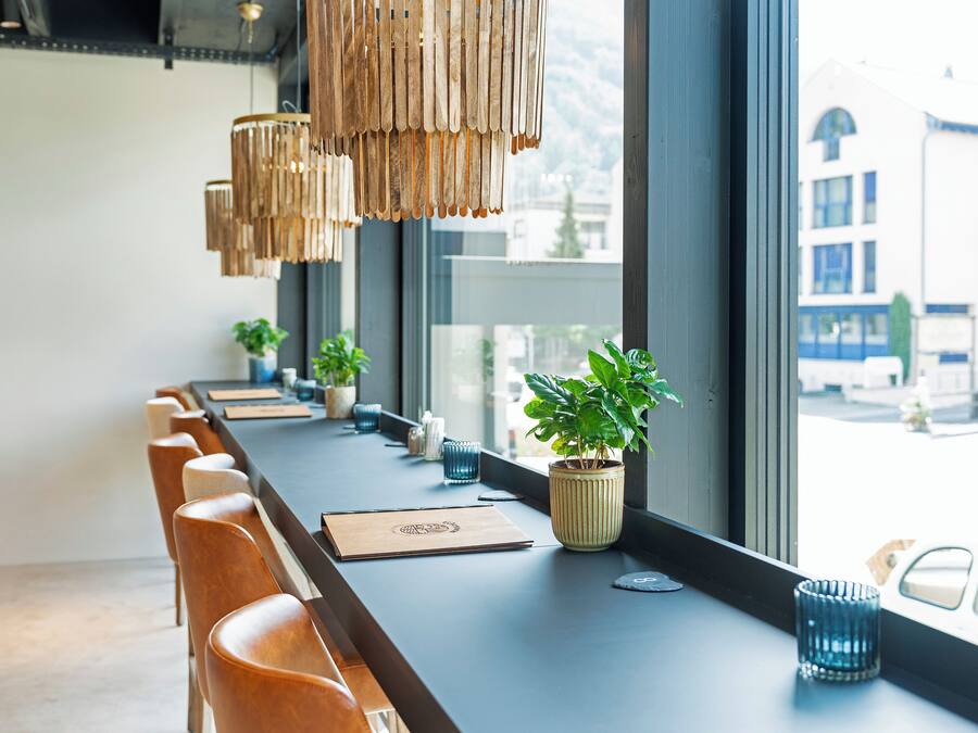 A long, dark wooden table with chairs, potted plants, and a small blue candle.
