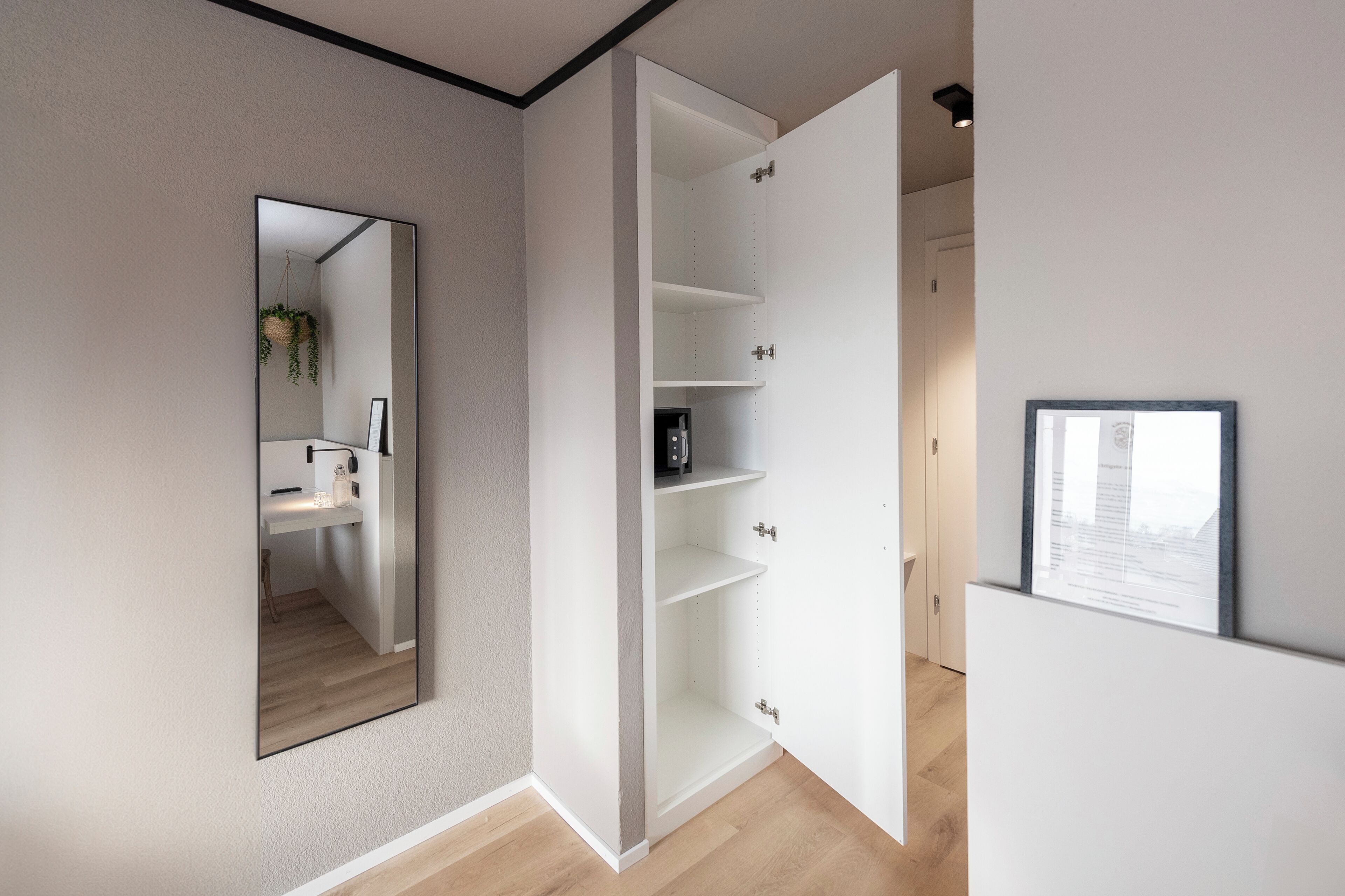 Una habitación moderna y minimalista con un espejo grande, un armario blanco con varios estantes y un cuadro en la pared.
