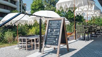 Un espace extérieur aménagé avec des tables et des chaises, un tableau noir servant de menu, des parasols et du mobilier de jardin.