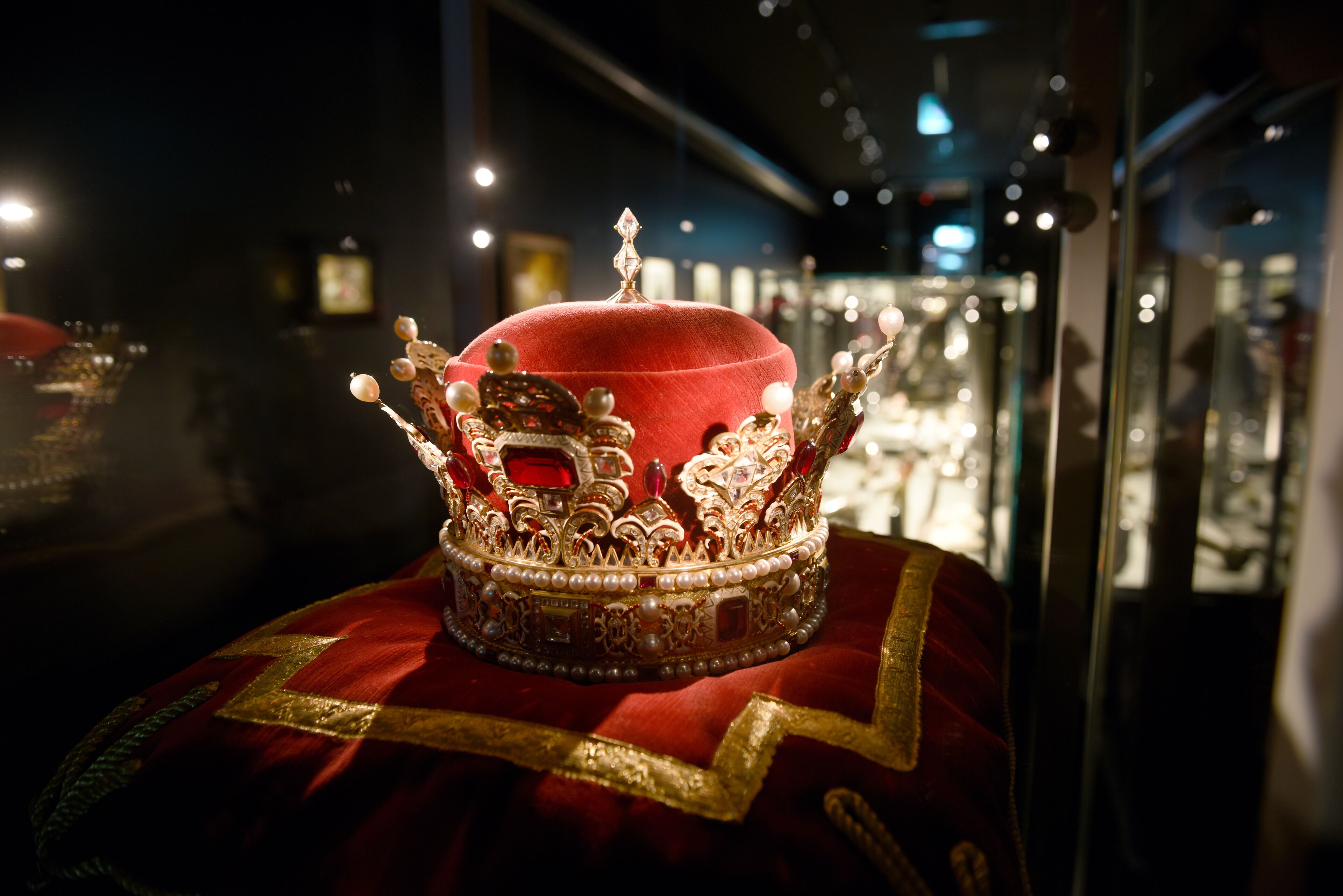 Eine Vitrine mit einem roten Samtobjekt, verziert mit Gold und Perlen, vermutlich ein historisches Artefakt.