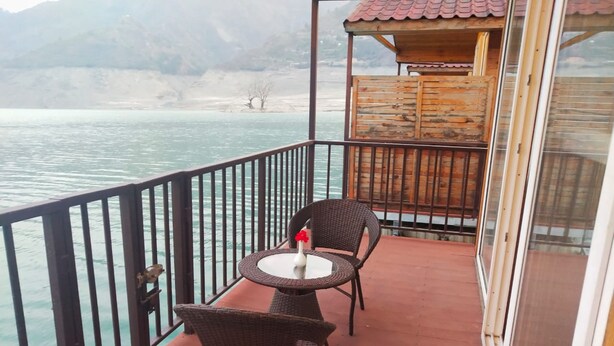 A balcony with two wicker chairs and a small table, overlooking a body of water and a mountainous landscape. - Le ROI Floating Huts & Eco Rooms (Tehri)