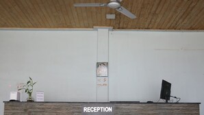 A reception desk with a wooden finish and a ceiling fan above. - Le ROI Floating Huts & Eco Rooms (Tehri)