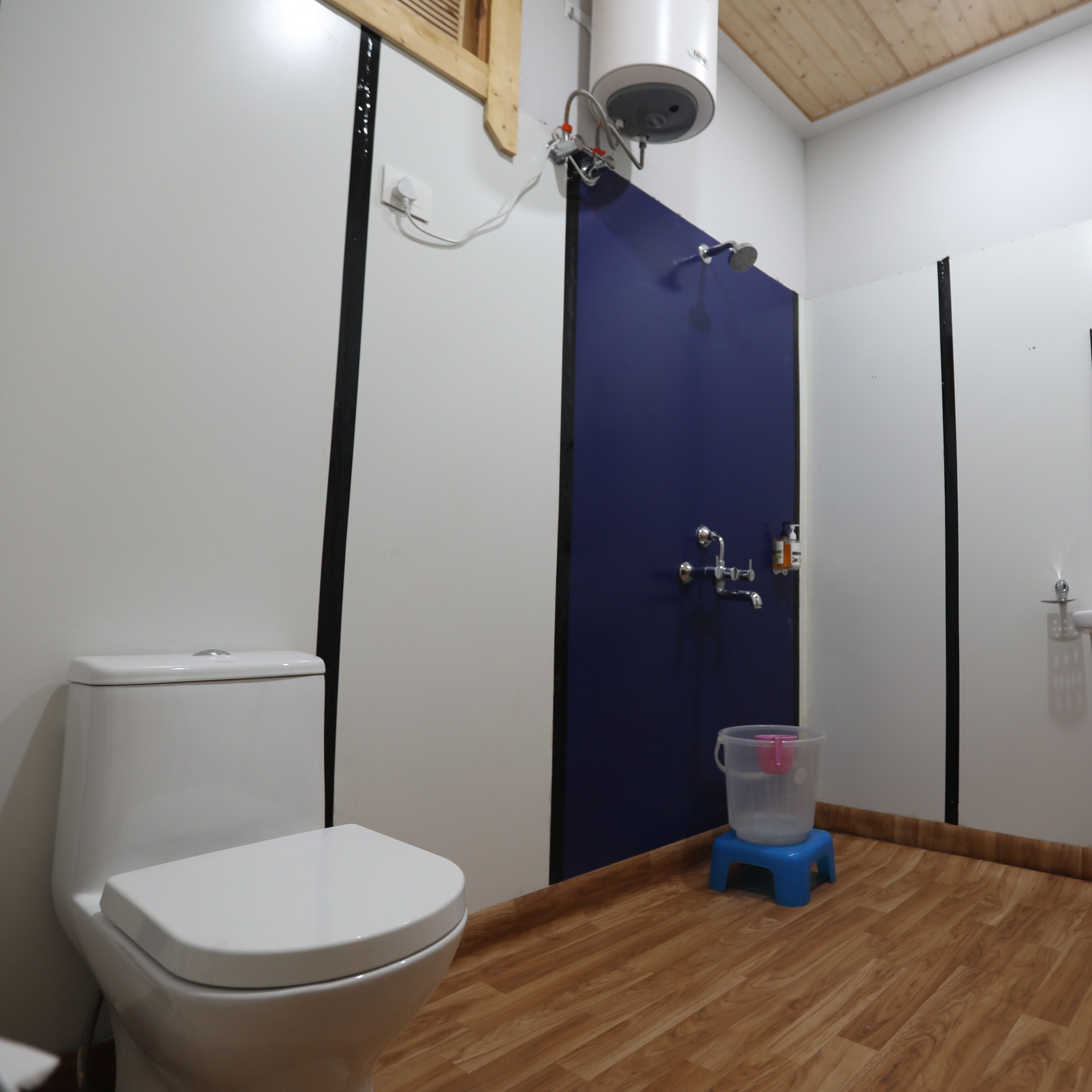 Ein Badezimmer mit einer weißen Toilette, einer blauen Duschkabine und einem Holzboden.