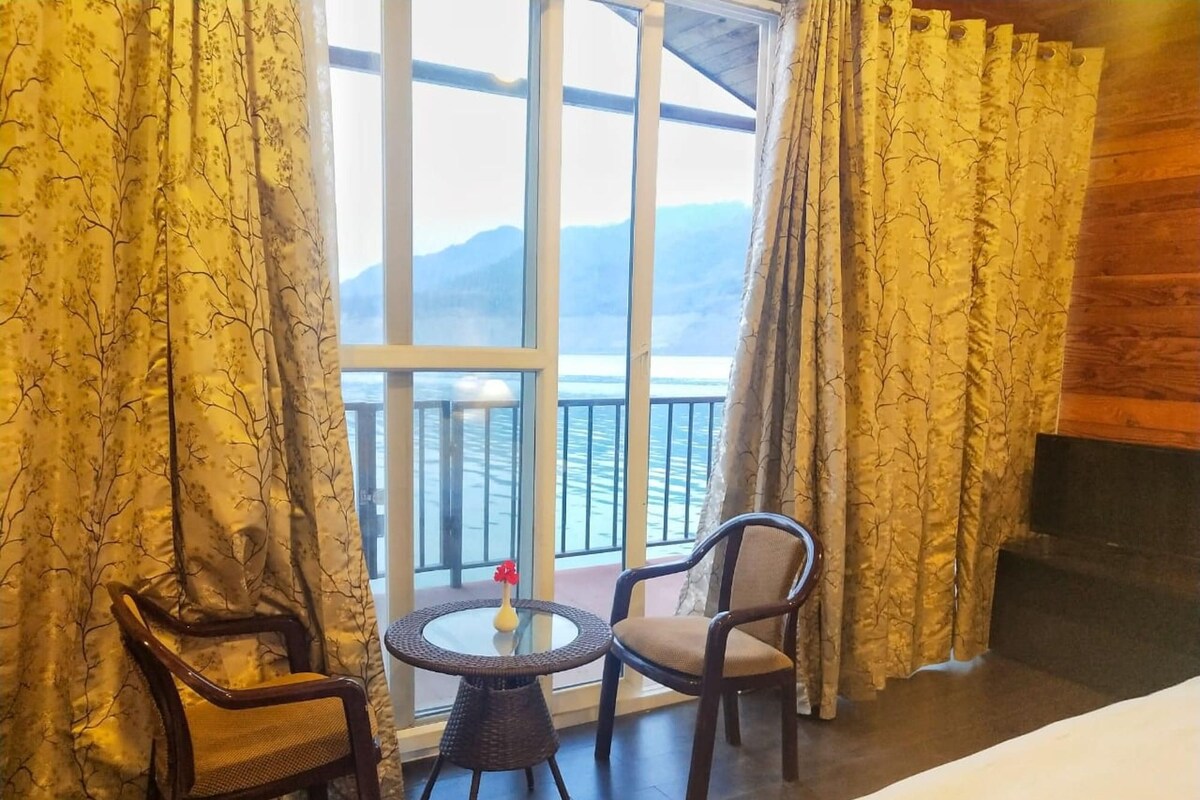 A room with a bed, two chairs, a small round table, and a large window with curtains.