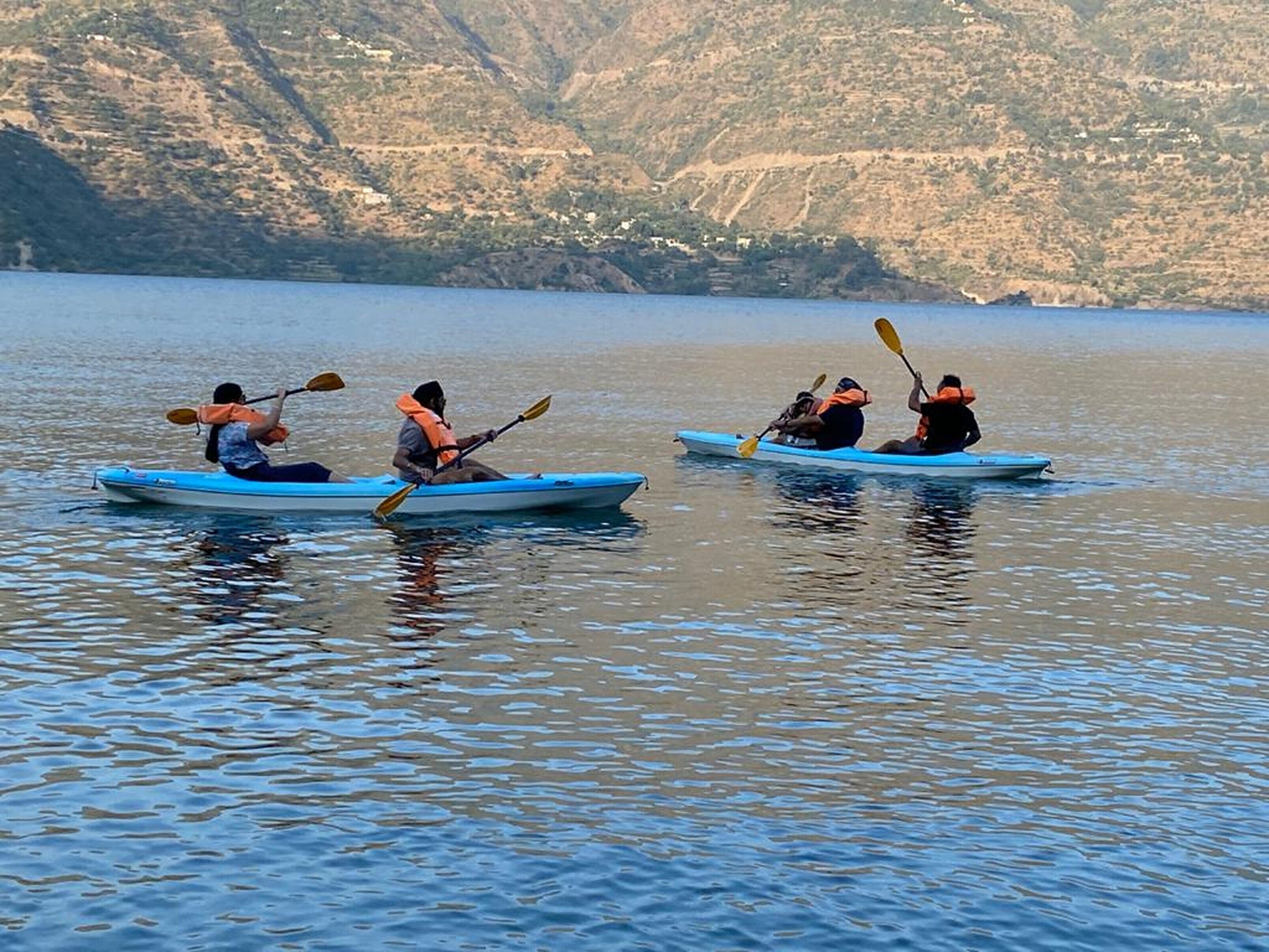 Three kayakers in blue kayaks on a calm lake with a mountainous backdrop.
