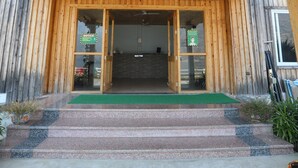 A wooden building entrance with a green mat, steps, and signs indicating social distancing measures. - Le ROI Floating Huts & Eco Rooms (Tehri)
