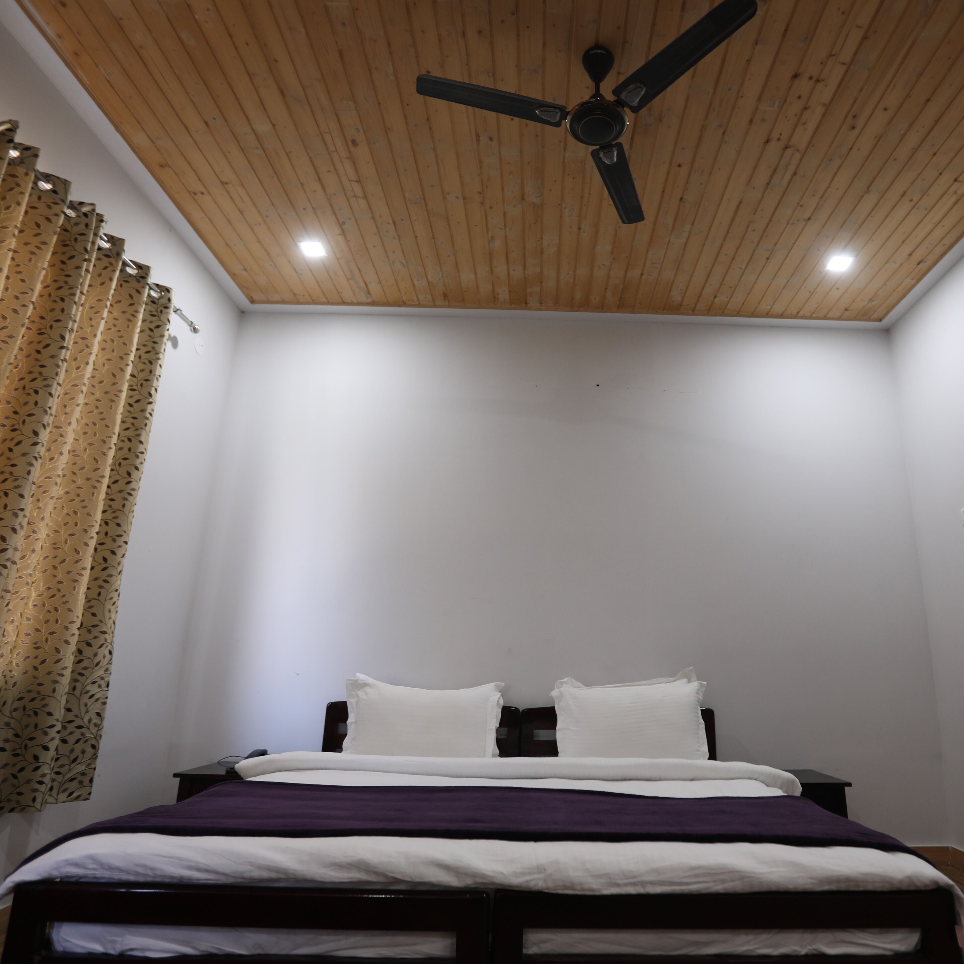 Ein Schlafzimmer mit Holzboden, einem Bett mit weißer und violetter Bettwäsche und einem Deckenventilator.
