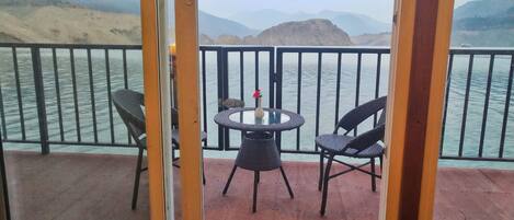 Un balcon avec une table et des chaises donnant sur une étendue d’eau et sur des montagnes lointaines.