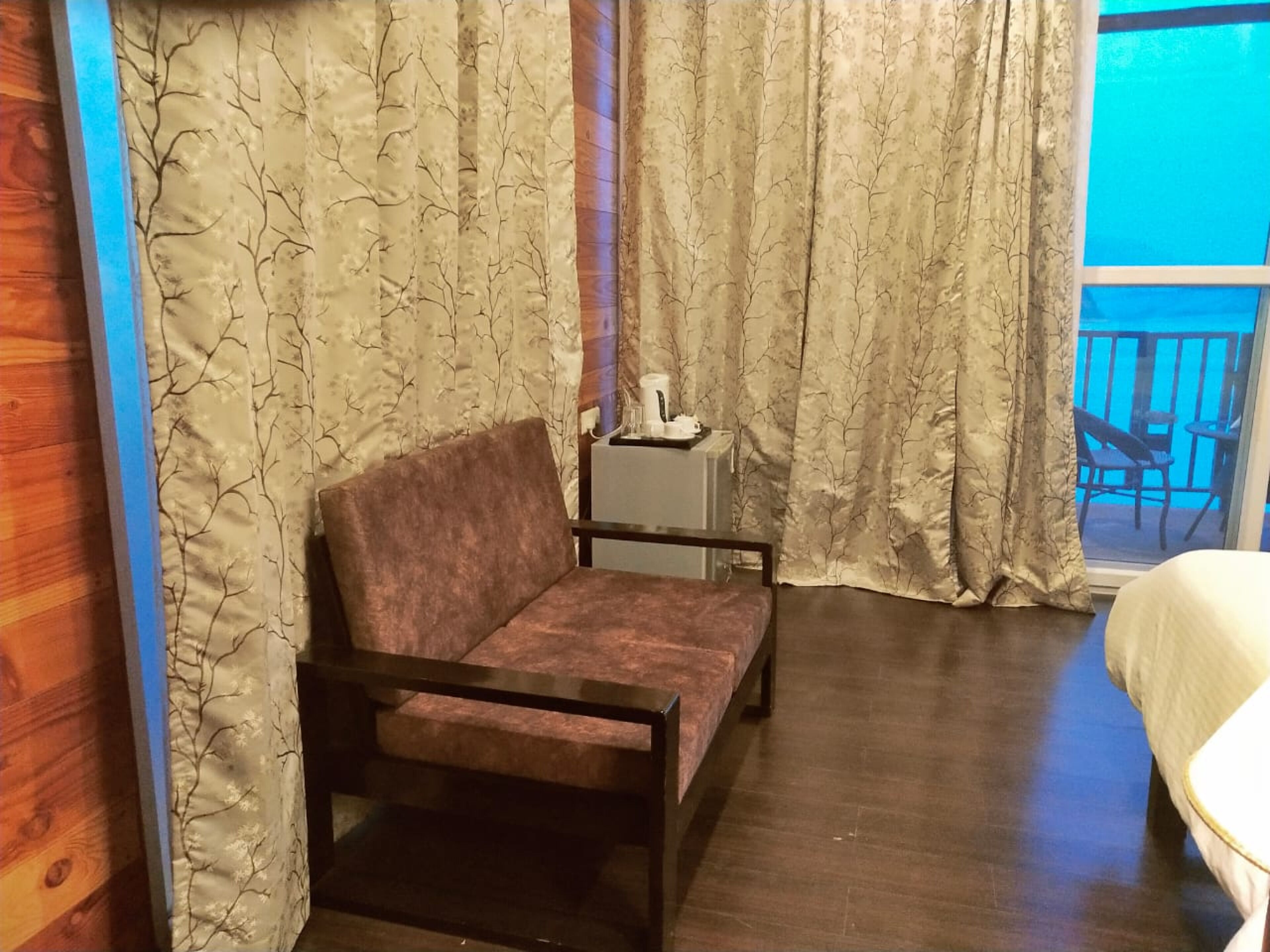 A room with a sofa, a small table with a lamp, and a view of a balcony.
