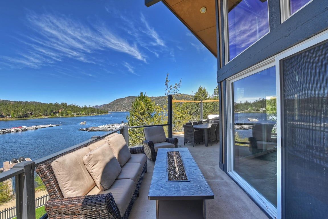 A balcony with a view of a lake, outdoor furniture, and a glass door leading to the interior.