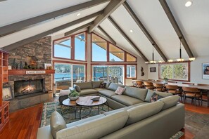 A spacious living area with a fireplace, large windows, and a high ceiling.