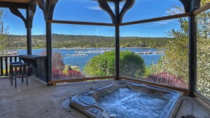 A hot tub in a covered outdoor area with a view of a lake and docked boats. - It's a Wonderful Life by Destination Big Bear : Luxury Deep Water Lakefront! Pool Table! Panoramic Lake & Mountain Views! HOT TUB! (Big Bear Lake CA)