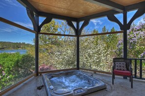 A hot tub in a covered outdoor area with a view of a lake and trees.