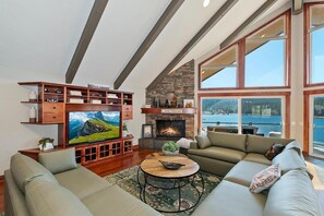 Una sala de estar con televisor, chimenea y un amplio ventanal con vista al agua.