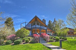 A modern two-story house with a balcony, surrounded by well-maintained gardens and trees.