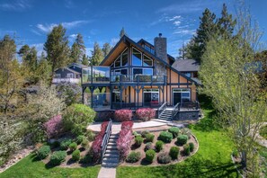 A modern two-story house with a large deck, surrounded by a well-maintained garden and trees.