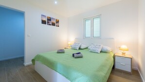 A bedroom with a green bedspread, two bedside lamps, a nightstand, and a window with blinds. - Villa Dundo Pero (Mljet)