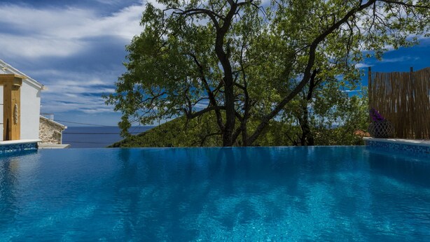 A clear blue infinity pool with a view of the sea, surrounded by a wooden fence and a tree. - Villa Dundo Pero (Mljet)