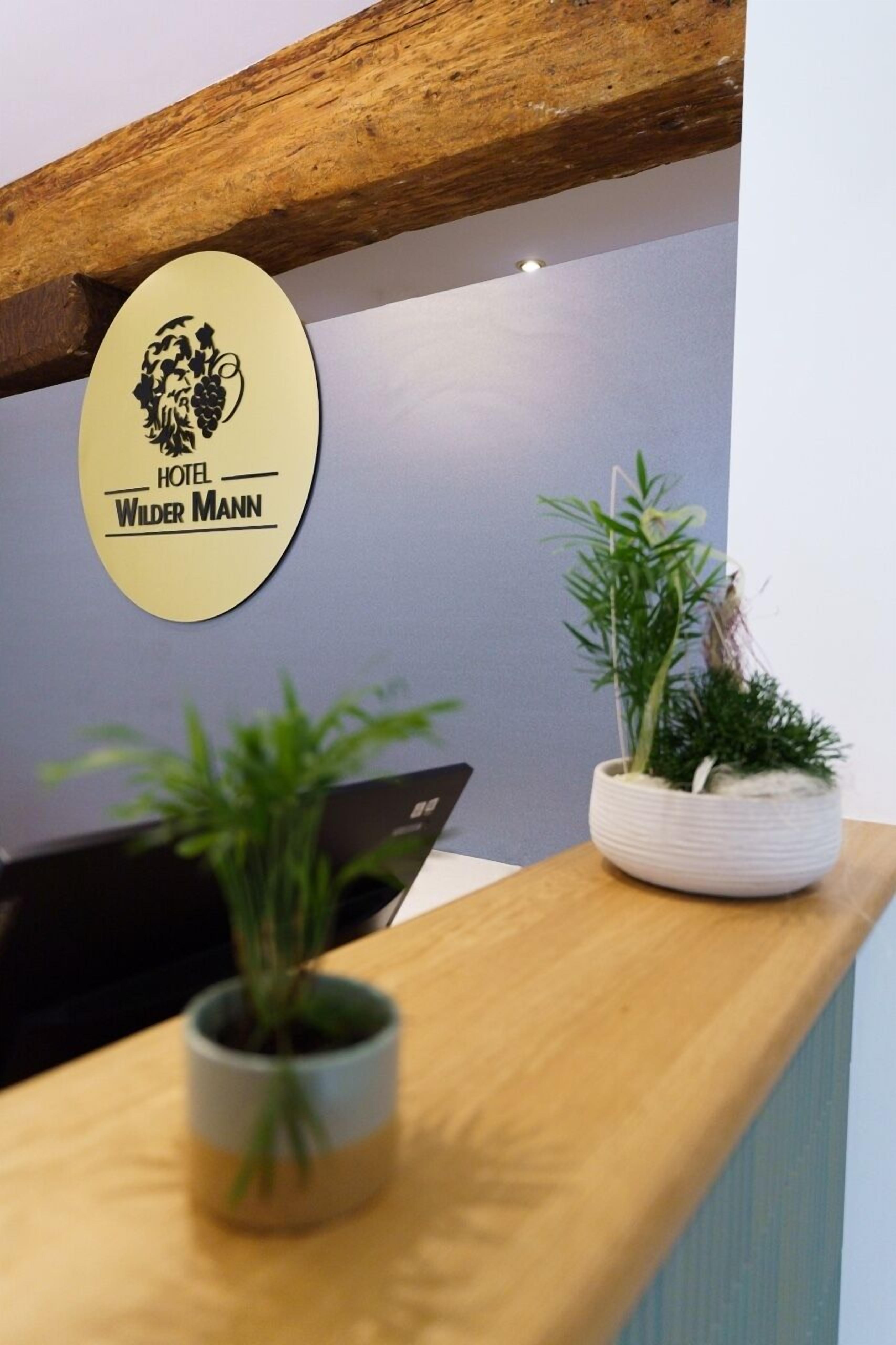 A reception desk with a sign for Hotel Wilder Mann, a wooden ceiling, and two potted plants.