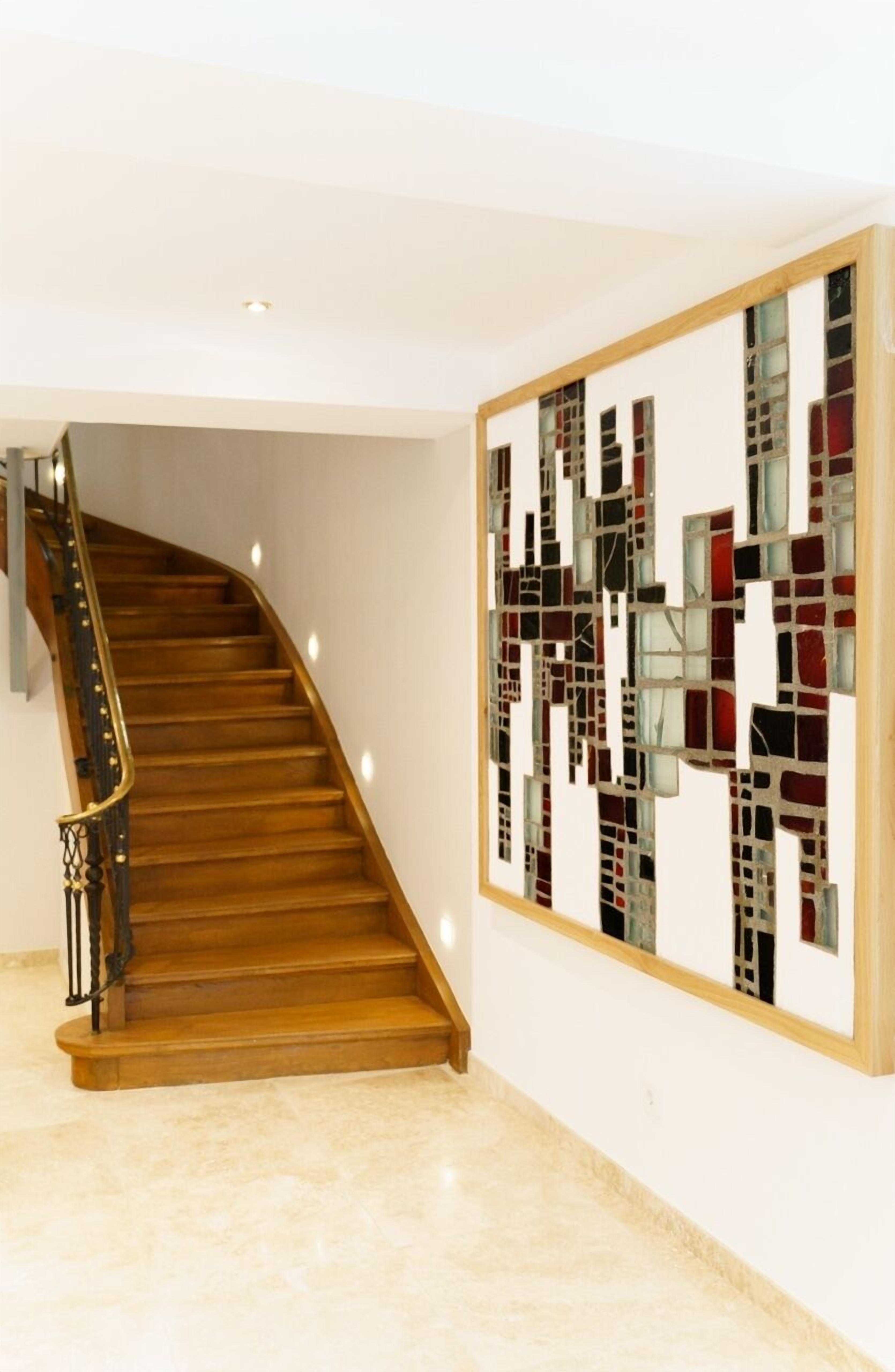 Eine Treppe mit Holzboden und Metallgeländer, die zu einem Raum führt, in dem ein großes abstraktes Kunstwerk an der Wand hängt.