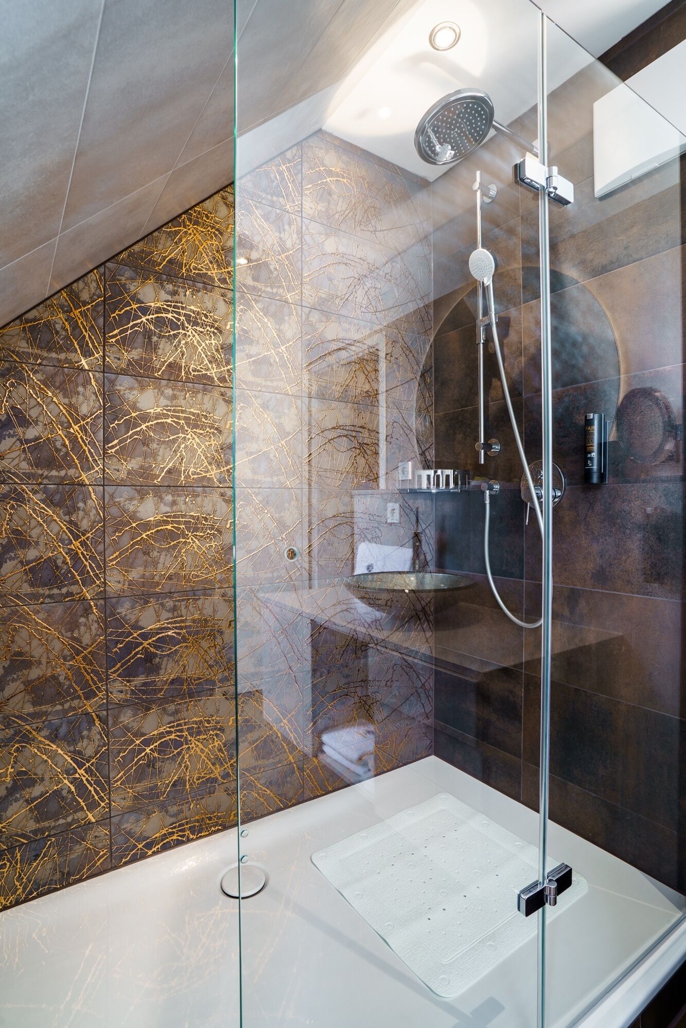 Una ducha moderna con cabina de vidrio, paredes de mármol y encimera blanca.