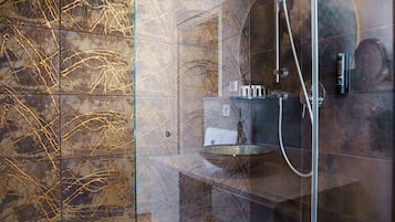 Una ducha moderna con cabina de vidrio, paredes de mármol y encimera blanca.