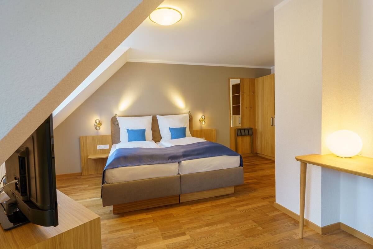 Un dormitorio moderno con techo inclinado, una cama grande, mesitas de noche, un televisor y un armario de madera.