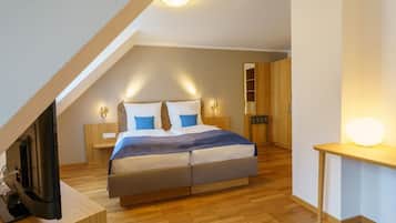 A modern bedroom with a sloped ceiling, a large bed, bedside tables, a TV, and a wooden wardrobe.