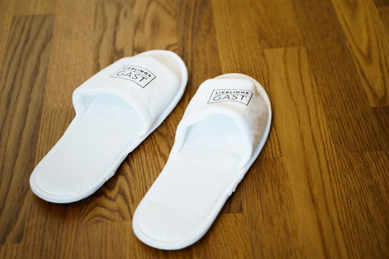 Une paire de pantoufles blanches avec l’inscription « LIEBLINGS GAST » sur la semelle intérieure.