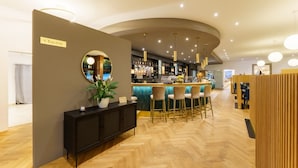 A modern hotel lobby with a bar area, a reception desk, and a seating area with a wooden floor.