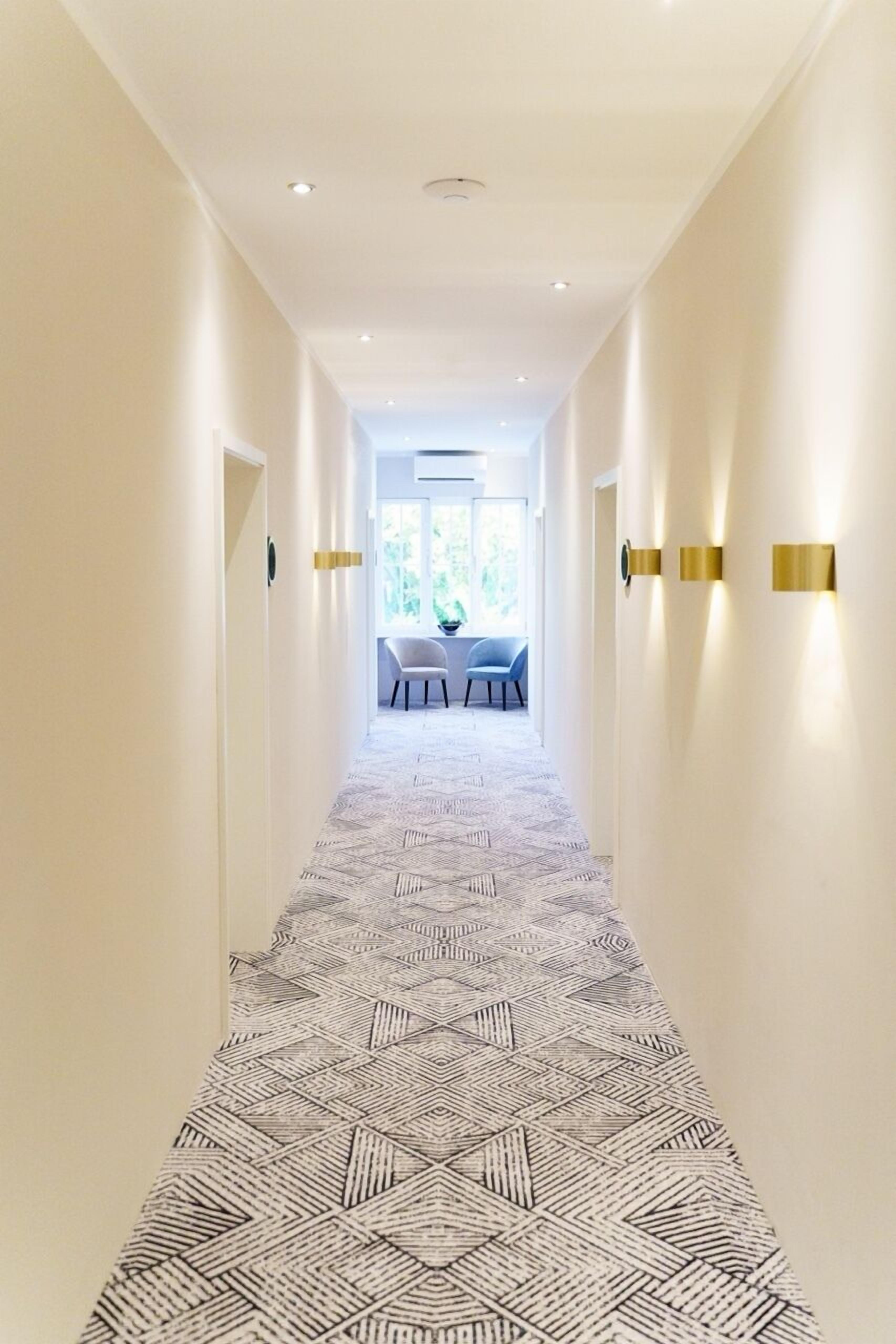 Un pasillo con alfombra de diseño geométrico, paredes blancas e iluminación empotrada.