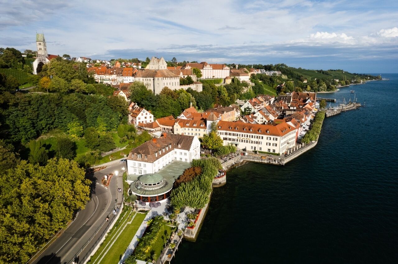 An aerial view of a riverside town with historic buildings, a prominent tower, and a well-maintained waterfront promenade.