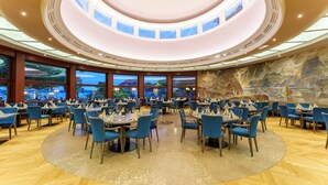 A spacious dining area with round tables and blue chairs, large windows, and a high ceiling with skylights.