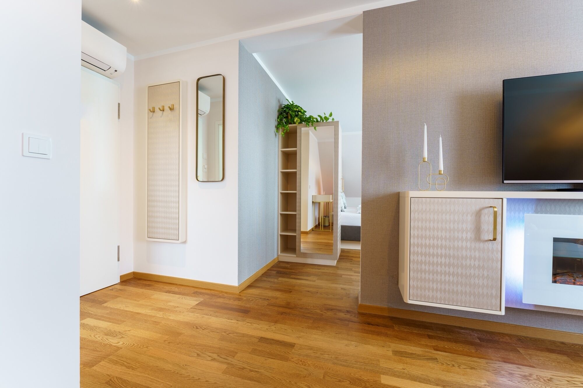 Una sala de estar moderna con televisor de pantalla plana, piso de madera, mueble empotrado y un espejo grande.