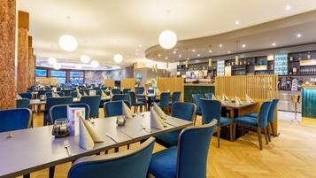 A modern restaurant with round tables, blue chairs, and a bar area.