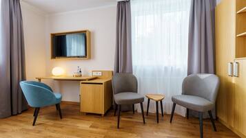 A modern hotel room with a wooden desk, two chairs, a small table, and a wardrobe.