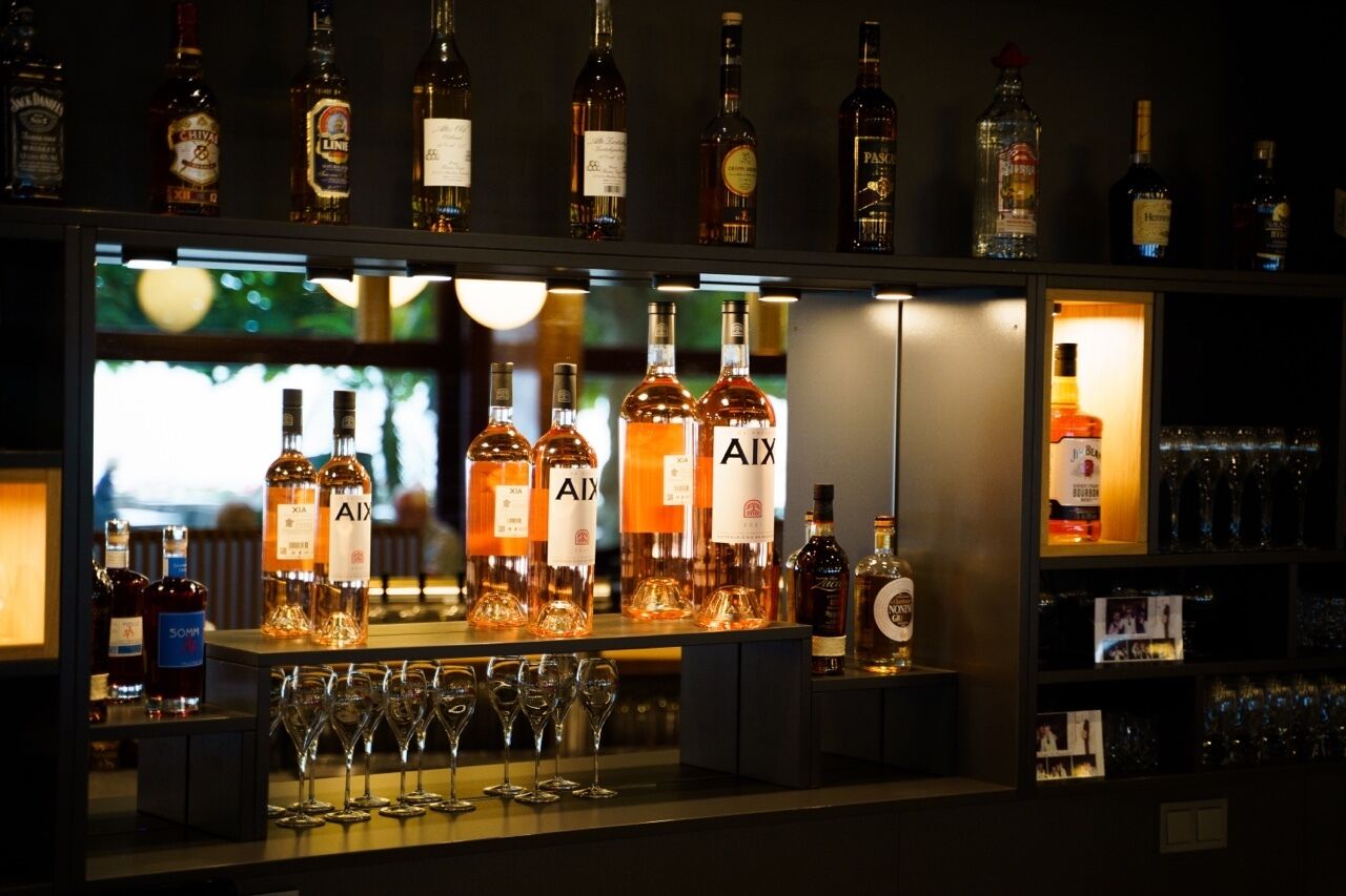 Un espace bar avec de nombreuses bouteilles d’alcool, dont une sélection bien visible de bouteilles de la marque « AIX », et plusieurs verres alignés sur le comptoir.