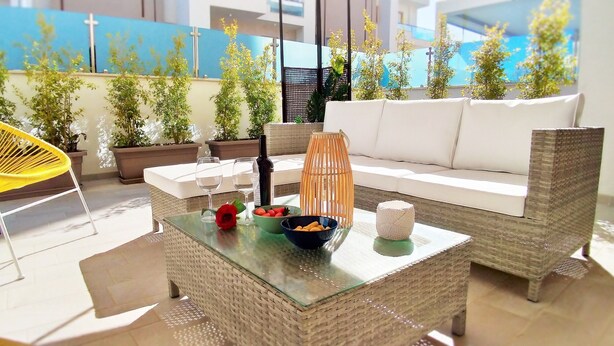 A modern outdoor seating area with wicker furniture, a glass coffee table, and potted plants.