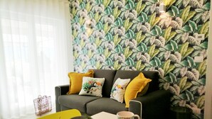 A living room with a sofa, cushions, a table with fruit, and a patterned wall.