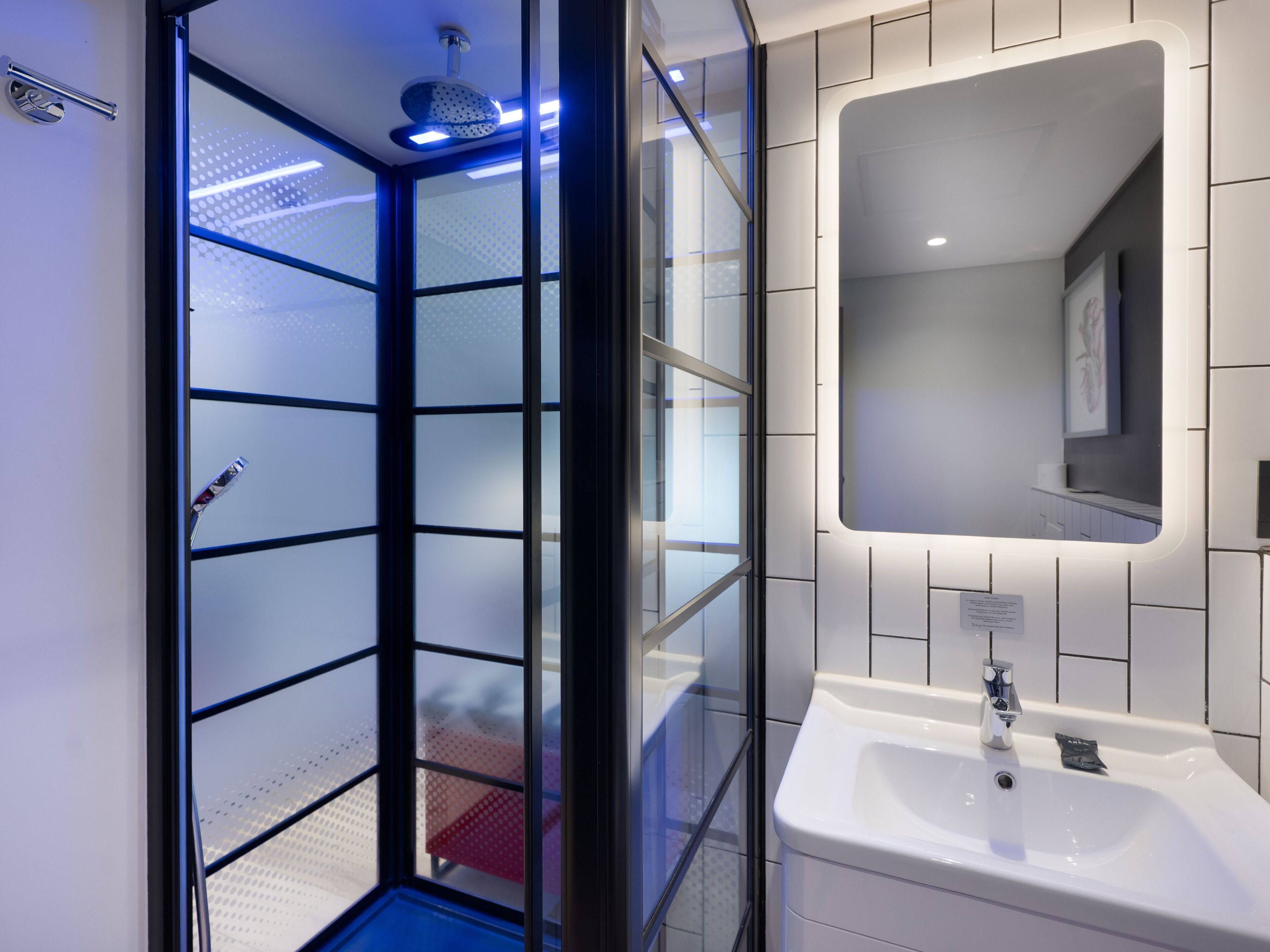 Un baño moderno con cabina de ducha de vidrio, un lavamanos blanco y un espejo.