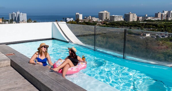 A rooftop pool with a city view, a glass barrier, and a wooden deck. - ANEW Hotel Green Point (Cape Town)