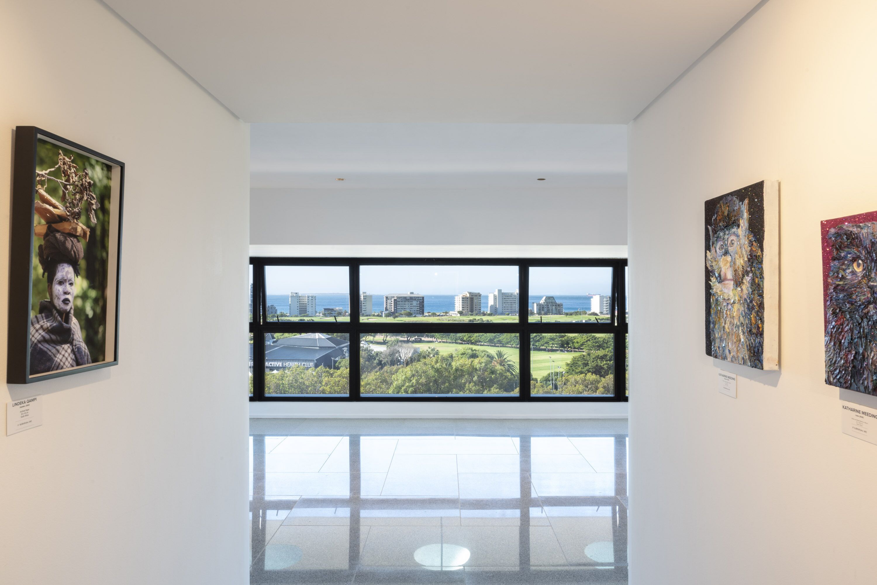 Una galería de arte con grandes ventanales que ofrecen vistas a edificios y espacios verdes.