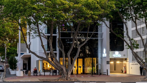 A modern hotel with a glass facade, outdoor seating area, and a visible entrance. - ANEW Hotel Green Point (Cape Town)