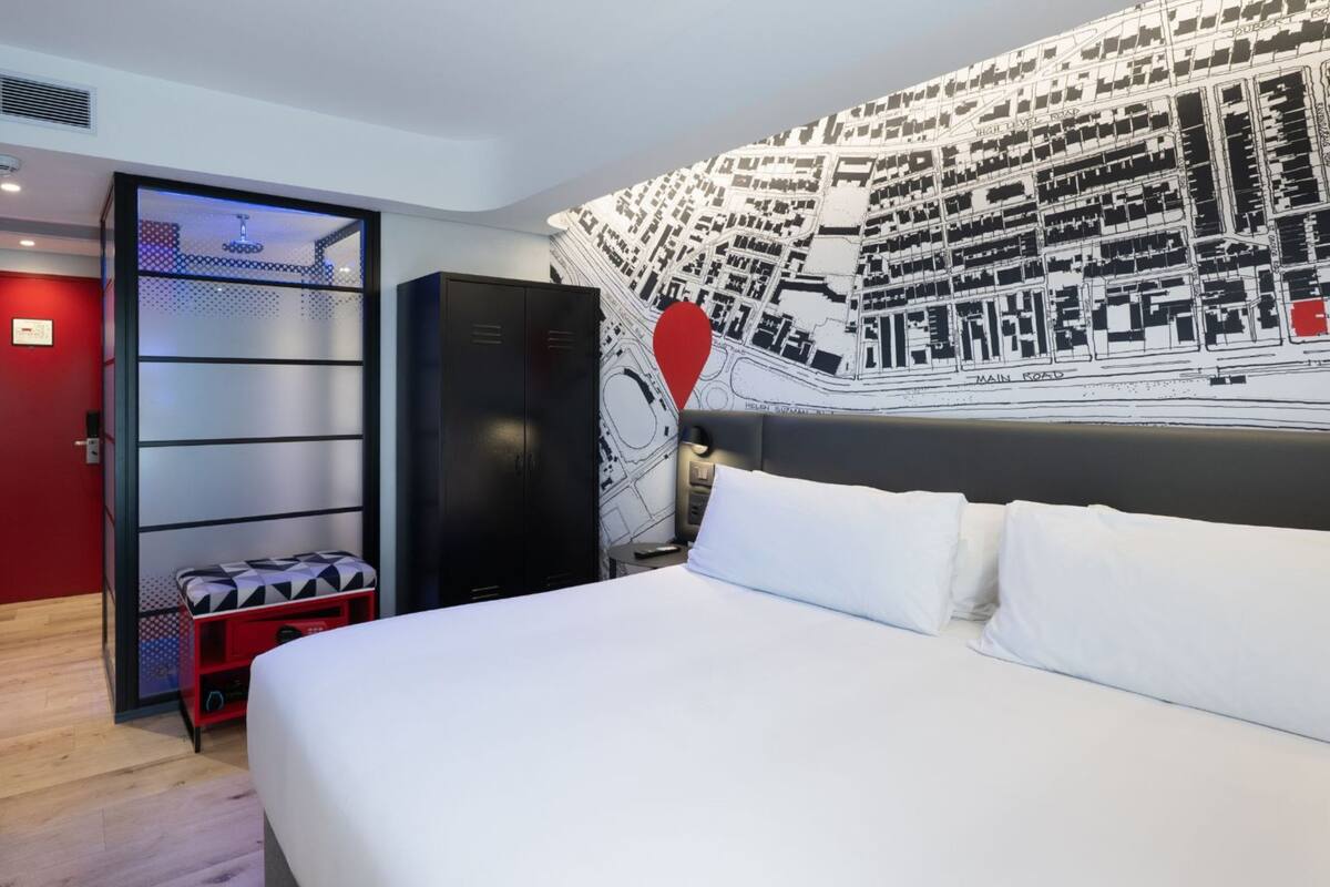 A hotel room with a large bed, a red bench, a wardrobe, and a wall map.